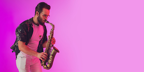 Image showing Young caucasian jazz musician playing the saxophone in neon light, flyer with copyspace for ad
