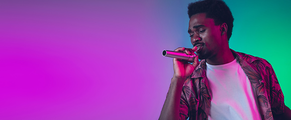 Image showing African-american male singer portrait isolated on gradient studio background in neon light, flyer with copyspace