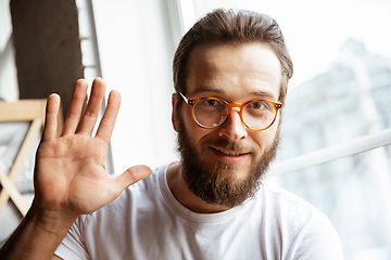 Image showing Caucasian musician greeting audience before online concert at home isolated and quarantined, cheerful, smiling