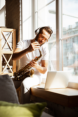 Image showing Caucasian musician playing saxophone during online concert at home isolated and quarantined, impressive improvising