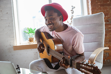 Image showing African-american musician playing guitar during online concert at home isolated and quarantined, impressive improvising