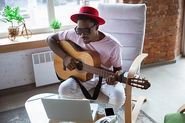 Image showing African-american musician playing guitar during online concert at home isolated and quarantined, impressive improvising