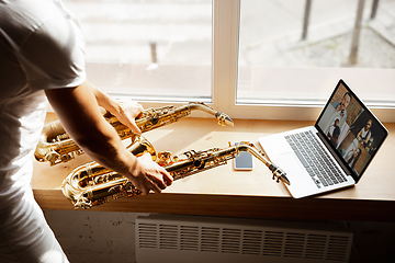 Image showing Caucasian musician playing saxophone during concert at home isolated and quarantined, impressive improvising with band connected online