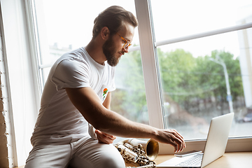 Image showing Caucasian musician preparing for concert at home isolated and quarantined, impressive improvising with band connected online