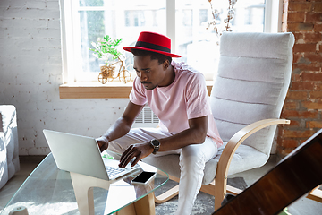 Image showing African-american musician typing text with laptop sitting at home, musician during quarantine and insulation