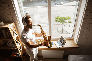 Image showing Caucasian musician playing saxophone during online concert at home isolated and quarantined, impressive improvising