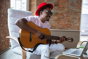 Image showing African-american musician playing guitar during online concert at home isolated and quarantined, impressive improvising
