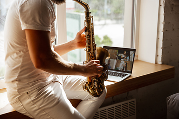 Image showing Caucasian musician playing saxophone during concert at home isolated and quarantined, impressive improvising with band connected online