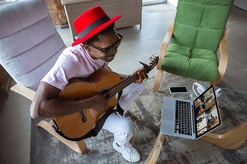 Image showing African-american musician playing guitar during online concert at home isolated and quarantined, impressive improvising