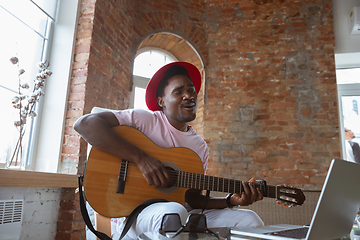 Image showing African-american musician playing guitar during online concert at home isolated and quarantined, impressive improvising