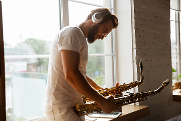 Image showing Caucasian musician choosing instrument for concert at home isolated and quarantined, impressive improvising with band connected online