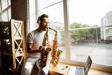 Image showing Caucasian musician playing saxophone during concert at home isolated and quarantined, impressive improvising with band connected online