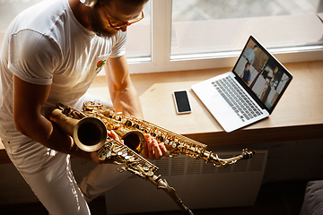 Image showing Caucasian musician playing saxophone during concert at home isolated and quarantined, impressive improvising with band connected online