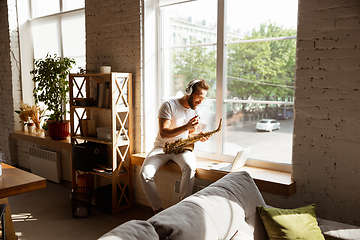 Image showing Caucasian musician playing saxophone during online concert at home isolated and quarantined, impressive improvising