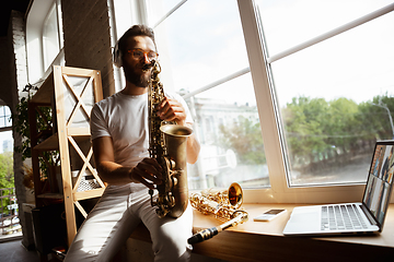 Image showing Caucasian musician playing saxophone during concert at home isolated and quarantined, impressive improvising with band connected online