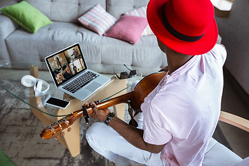 Image showing African-american musician playing guitar during concert at home isolated and quarantined, impressive improvising with band connected online