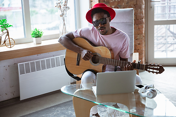 Image showing African-american musician playing guitar during online concert at home isolated and quarantined, impressive improvising