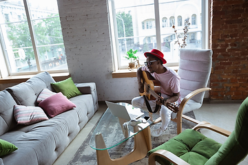 Image showing African-american musician playing guitar during online concert at home isolated and quarantined, impressive improvising