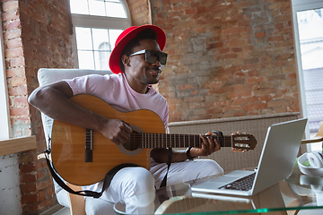 Image showing African-american musician playing guitar during online concert at home isolated and quarantined, impressive improvising