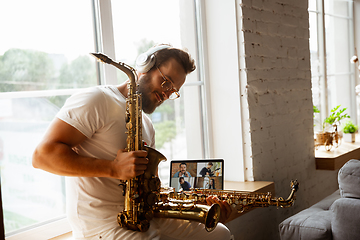 Image showing Caucasian musician preparing for concert at home isolated and quarantined, impressive improvising with band connected online