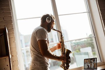 Image showing Caucasian musician playing saxophone during online concert at home isolated and quarantined, impressive improvising