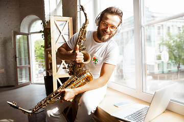 Image showing Caucasian musician choosing instrument for concert at home isolated and quarantined, impressive improvising with band connected online