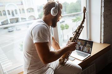 Image showing Caucasian musician playing saxophone during online concert at home isolated and quarantined, impressive improvising