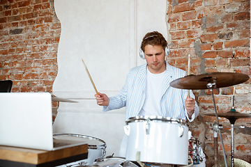 Image showing Caucasian musician playing drumms during online concert with the band at home isolated and attented, smiling, cheerful