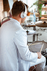 Image showing Caucasian musician playing drumms during online concert with the band at home isolated and attented, smiling, cheerful