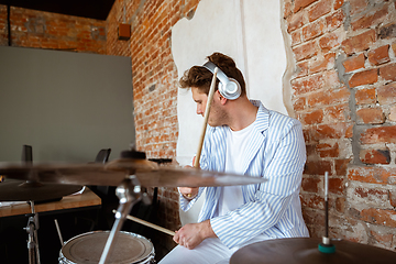 Image showing Caucasian musician playing drumms during online concert with the band at home isolated and attented, smiling, cheerful