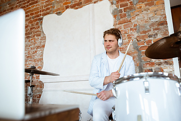 Image showing Caucasian musician playing drumms during online concert with the band at home isolated and attented, smiling, cheerful
