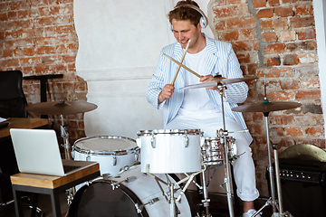 Image showing Caucasian musician playing drumms during online concert with the band at home isolated and attented, smiling, cheerful