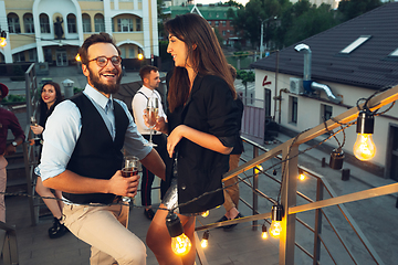 Image showing Corporate celebrating in the warm light of the lamps in summer evening, young friends, colleagues look happy, talk, have fun