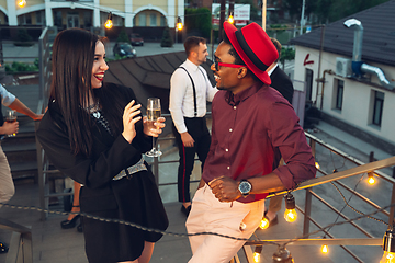 Image showing Corporate celebrating in the warm light of the lamps in summer evening, young friends, colleagues look happy, talk, have fun