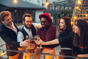 Image showing Corporate celebrating in the warm light of the lamps in summer evening, young friends, colleagues look happy, talk, have fun, cheers