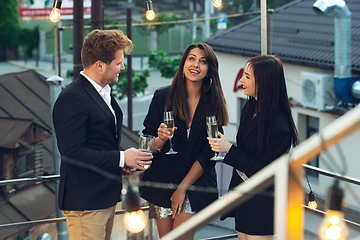 Image showing Corporate celebrating in the warm light of the lamps in summer evening, young friends, colleagues look happy, talk, have fun