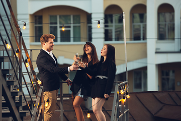 Image showing Corporate celebrating in the warm light of the lamps in summer evening, young friends, colleagues look happy, talk, have fun