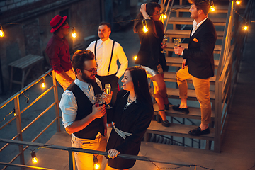 Image showing Corporate celebrating in the warm light of the lamps in summer evening, young friends, colleagues look happy, talk, have fun