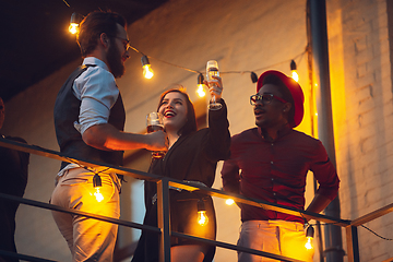 Image showing Corporate celebrating in the warm light of the lamps in summer evening, young friends, colleagues look happy, talk, have fun