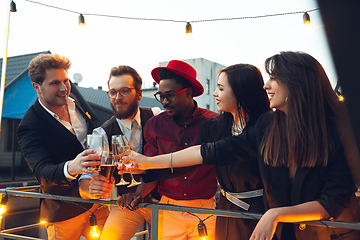 Image showing Corporate celebrating in the warm light of the lamps in summer evening, young friends, colleagues look happy, talk, have fun, cheers