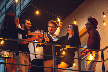 Image showing Corporate celebrating in the warm light of the lamps in summer evening, young friends, colleagues look happy, talk, have fun, cheers