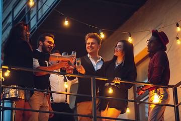 Image showing Corporate celebrating in the warm light of the lamps in summer evening, young friends, colleagues look happy, talk, have fun, cheers