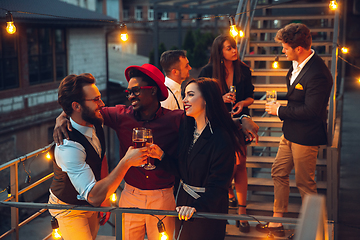 Image showing Corporate celebrating in the warm light of the lamps in summer evening, young friends, colleagues look happy, talk, have fun