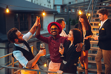 Image showing Corporate celebrating in the warm light of the lamps in summer evening, young friends, colleagues look happy, talk, have fun