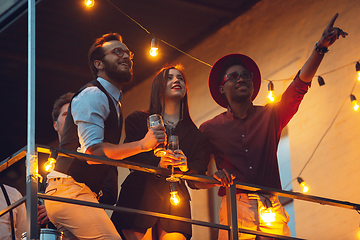 Image showing Corporate celebrating in the warm light of the lamps in summer evening, young friends, colleagues look happy, talk, have fun