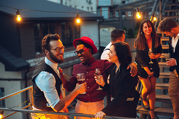 Image showing Corporate celebrating in the warm light of the lamps in summer evening, young friends, colleagues look happy, talk, have fun