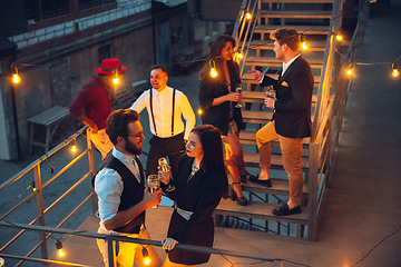 Image showing Corporate celebrating in the warm light of the lamps in summer evening, young friends, colleagues look happy, talk, have fun