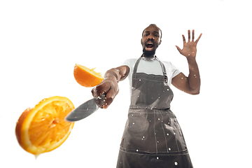Image showing Amazing african-american man preparing unbelievable food with close up action, details and bright emotions, professional cook. Cutting orange on the fly