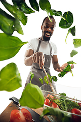 Image showing Amazing african-american man preparing unbelievable food with close up action, details and bright emotions, professional cook. Adding salad greens on the fly