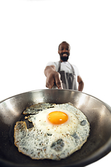 Image showing Amazing african-american man preparing unbelievable food with close up action, details and bright emotions, professional cook. Preparing fried eggs